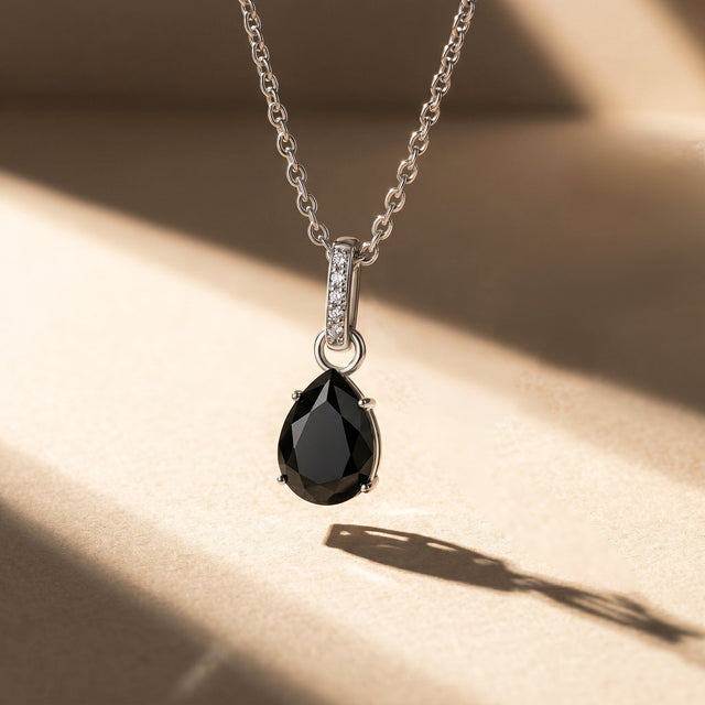 A silver black onyx necklace casts a long angled shadow across a pale stone surface.