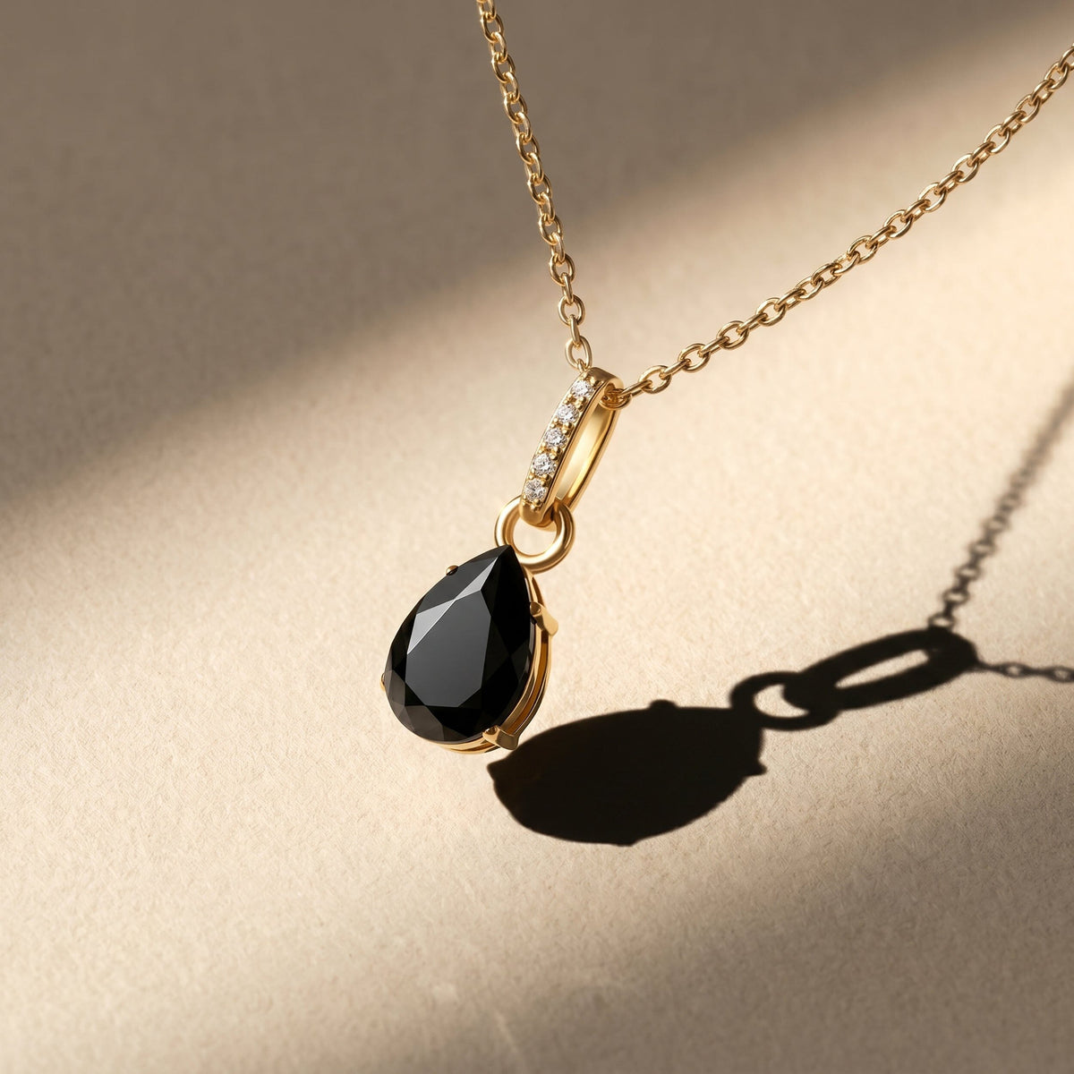 A yellow gold vermeil chain and black pear-shaped pendant appear above a warm stone tabletop in sunlight.