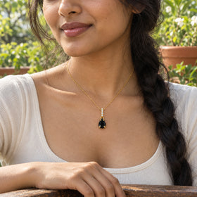 A woman with a dark braid wears the yellow gold vermeil black onyx necklace beside a wooden terrace railing.