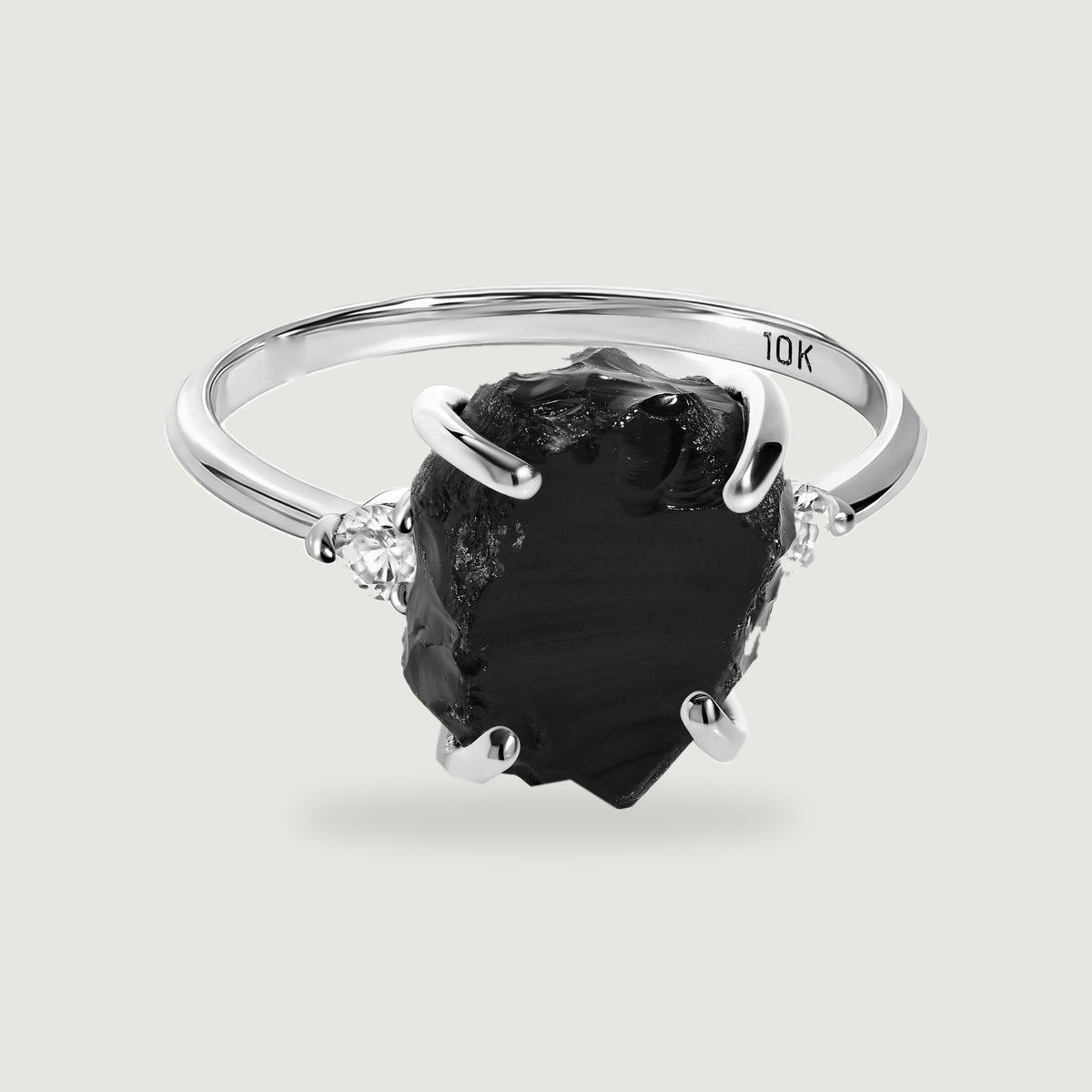 A white gold ring with an irregular black center stone and two clear side stones rests above a soft shadow.