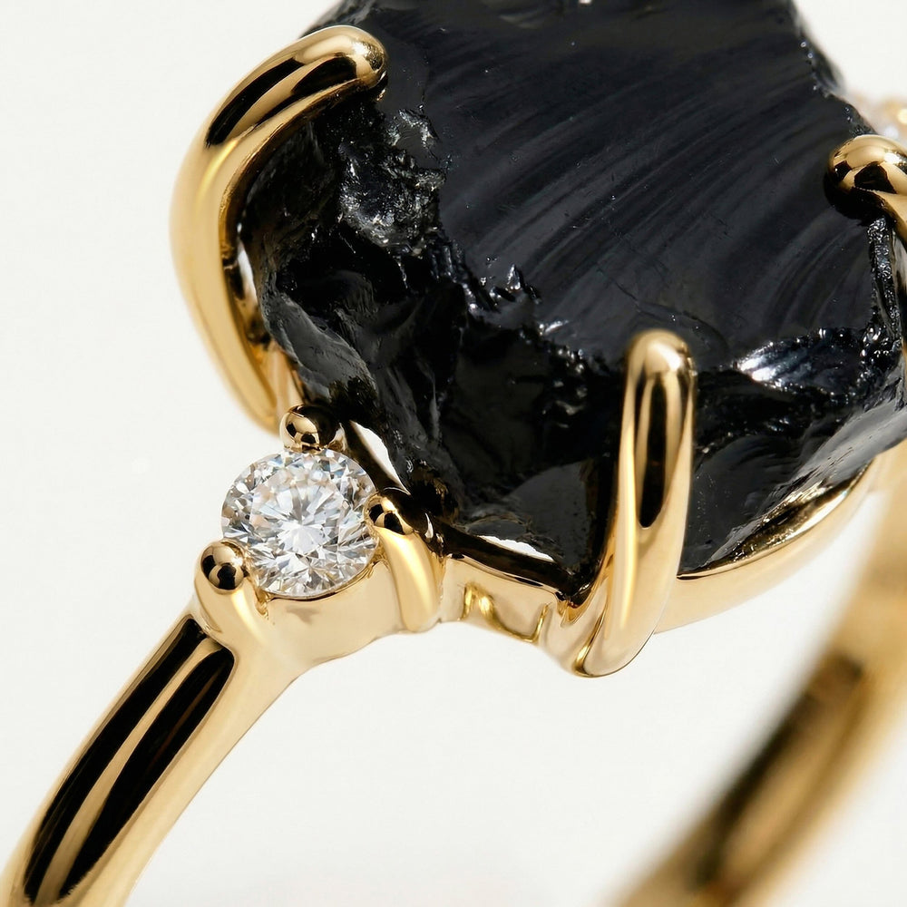A close view shows a clear round side stone beside the rough black stone and polished yellow gold prongs.