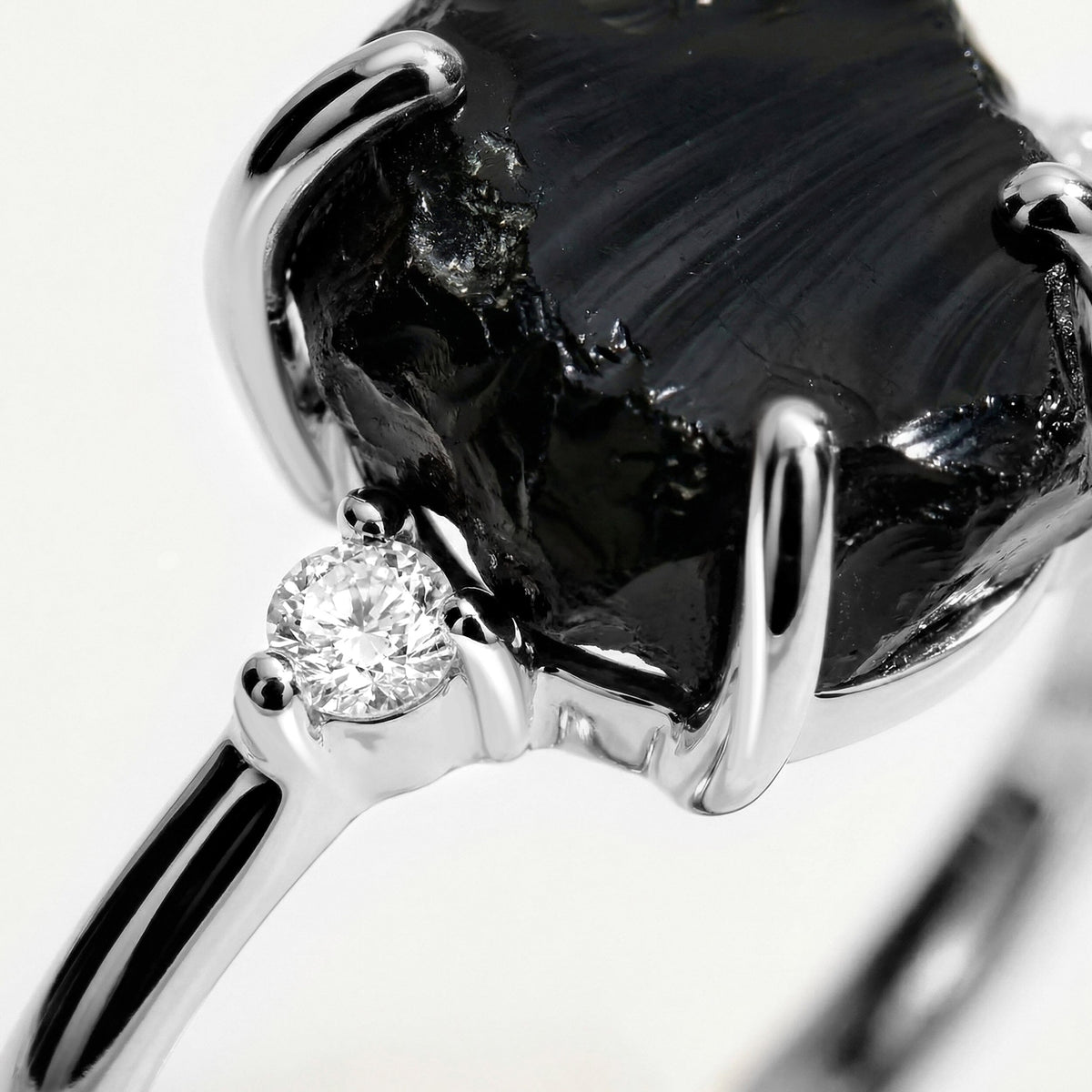 The white gold setting surrounds a textured black stone with a round clear accent visible beside it.