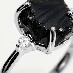 The white gold setting surrounds a textured black stone with a round clear accent visible beside it.