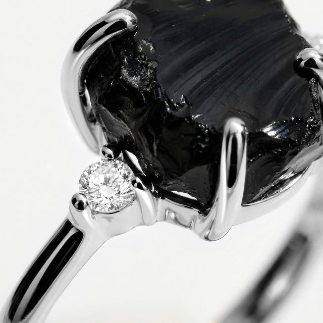 The white gold setting surrounds a textured black stone with a round clear accent visible beside it.