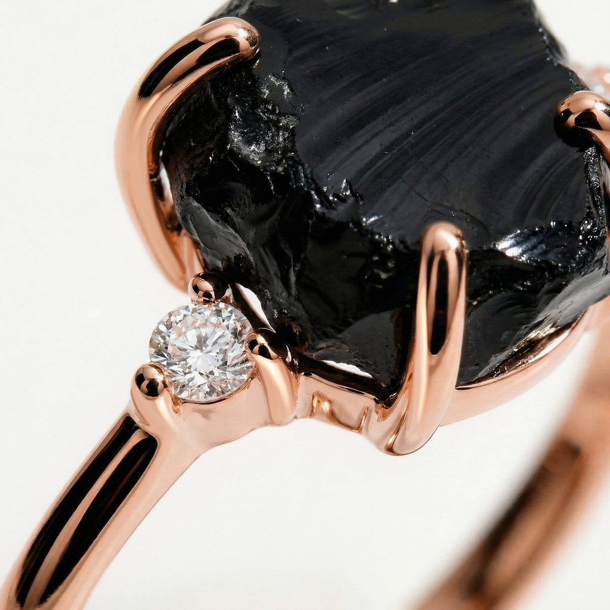 Polished rose gold prongs curve over the uneven black stone next to a sparkling round clear stone.