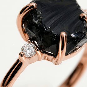 Polished rose gold prongs curve over the uneven black stone next to a sparkling round clear stone.