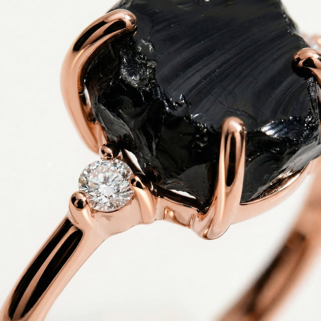 Polished rose gold prongs curve over the uneven black stone next to a sparkling round clear stone.
