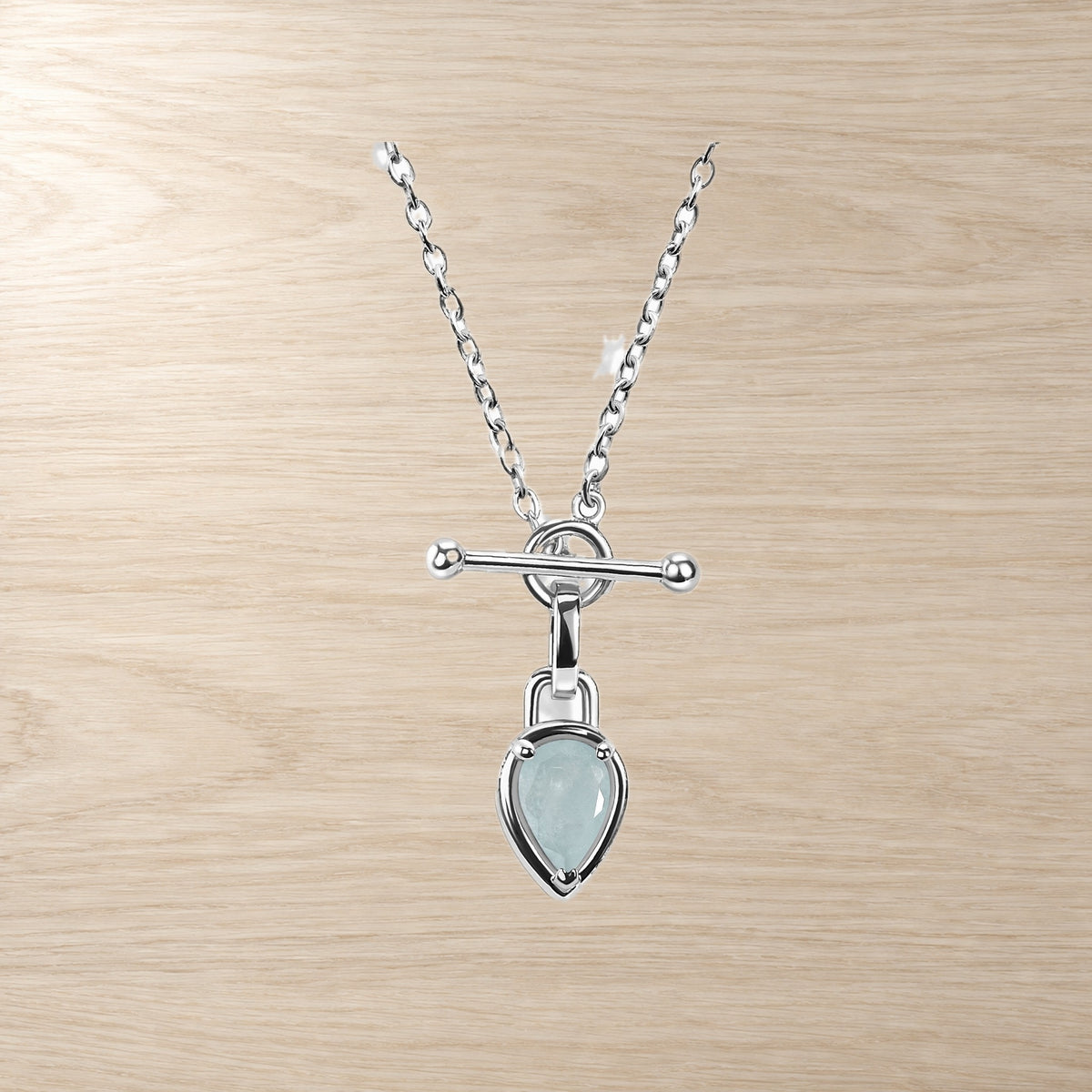 Close-up necklace with a pale blue pear-shaped stone, circular link, horizontal bar, and fine chain on wood.