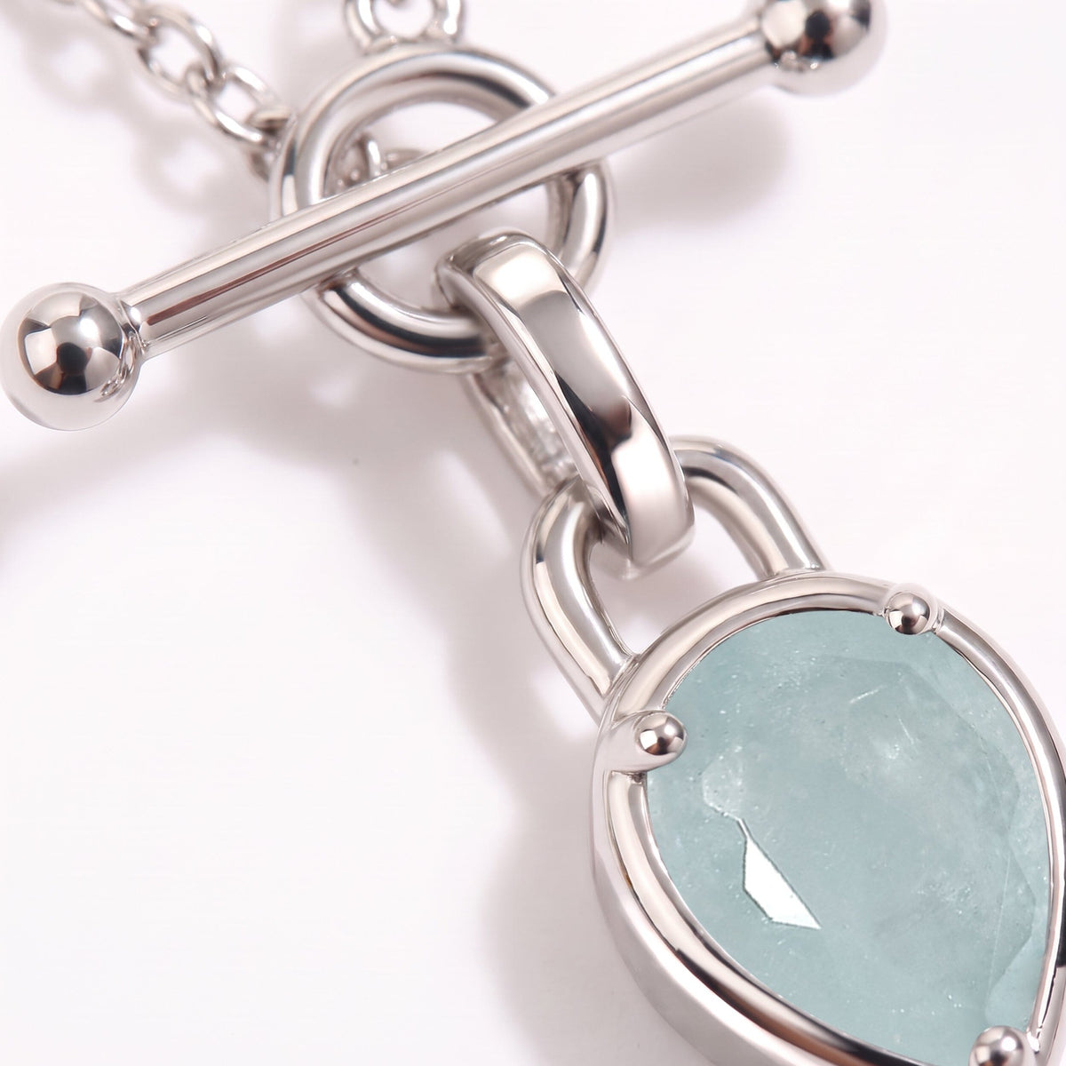 Macro view of the horizontal toggle bar, round ends, connecting ring, and faceted pale blue pendant.