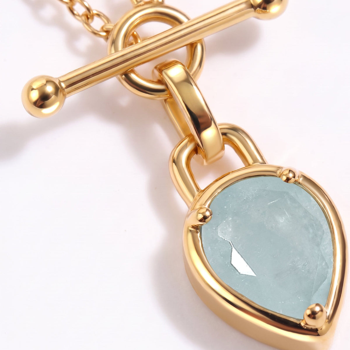 Detailed pendant close-up featuring a smooth bar clasp, circular links, and a pale blue faceted stone.