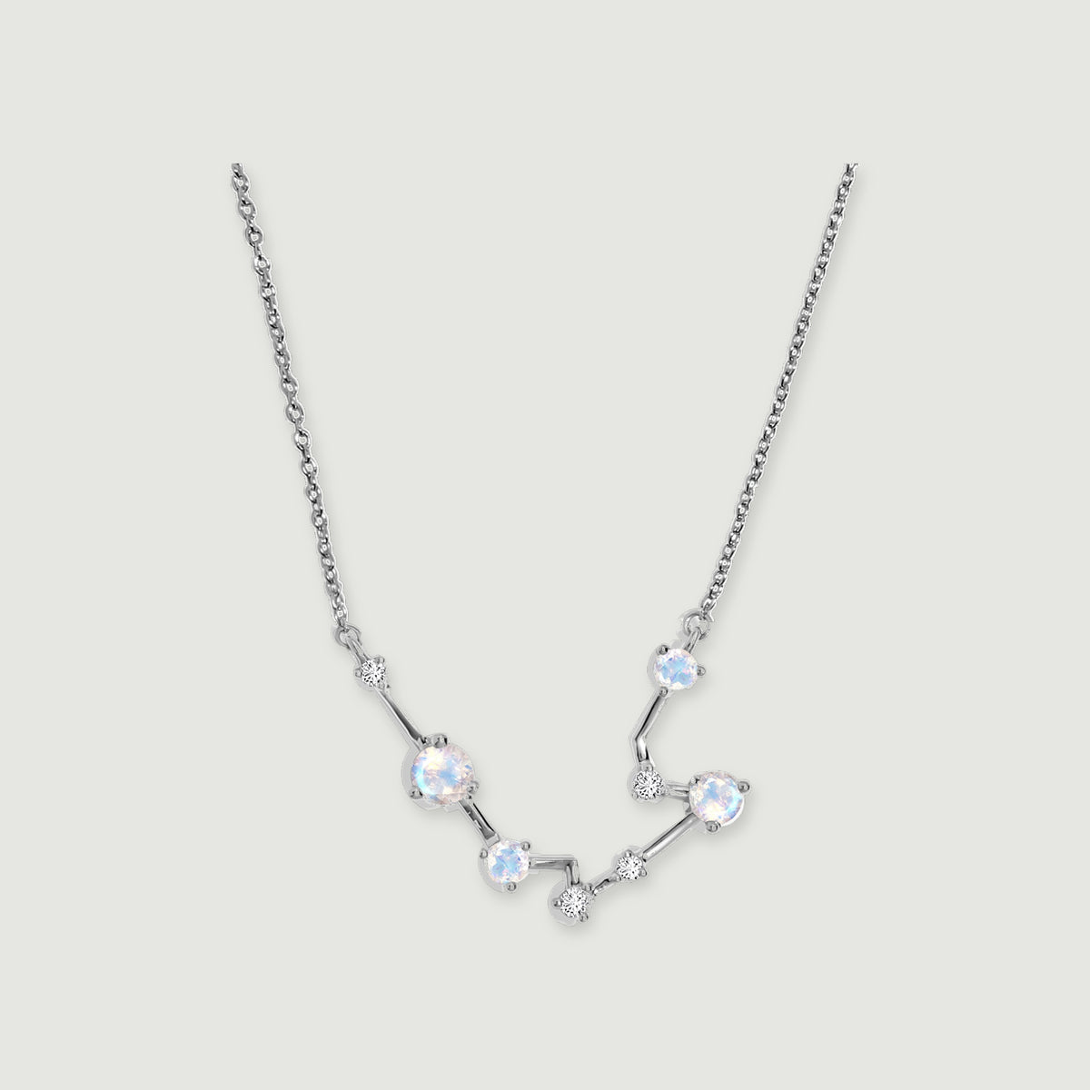 A silver chain frames a curved constellation of four round moonstones and small clear stones on a light gray background.