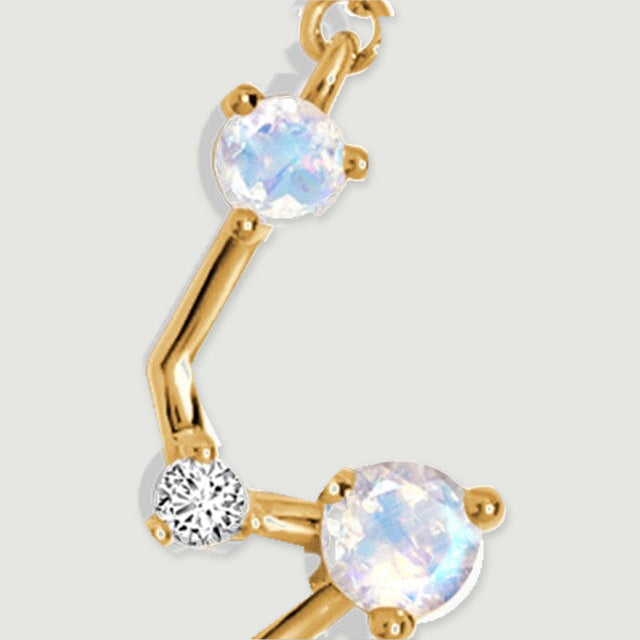Two round moonstones and a clear accent meet at the angled right side of the gold pendant.