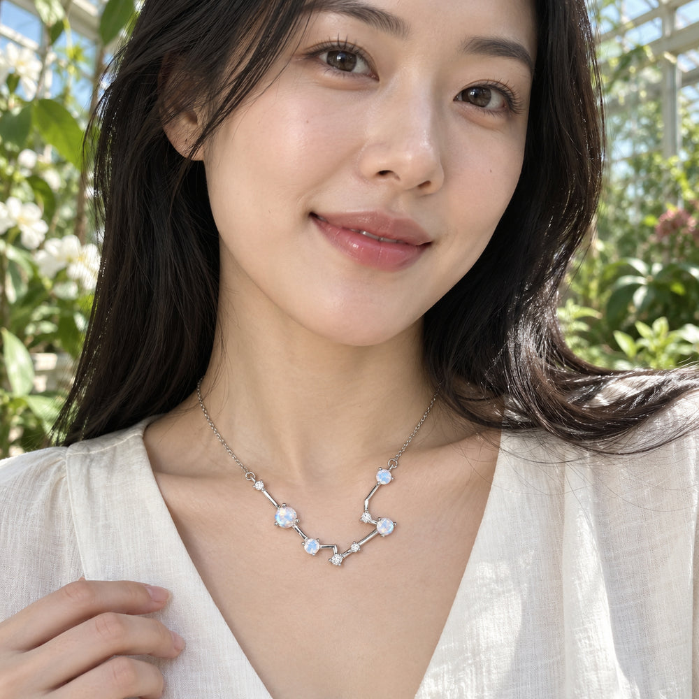A woman in a cream blouse wears the silver constellation necklace among green leaves in a glass conservatory.