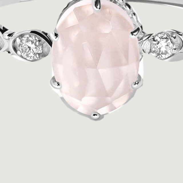 A close view shows the pale pink stone facets, polished white gold prongs, and the diamond settings along the left shoulder.