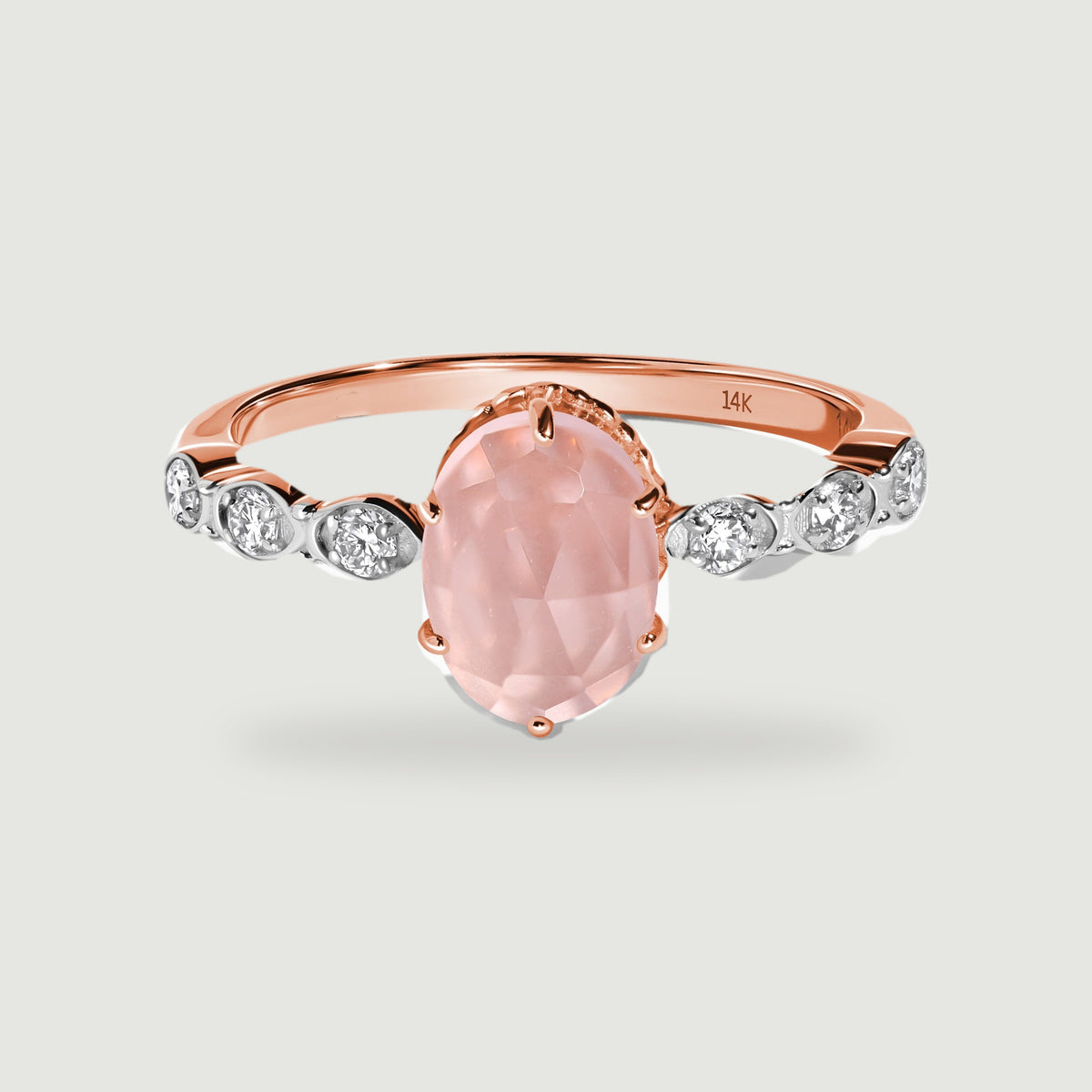A rose gold ring with a faceted oval pink center stone and six diamond accents is centered above a soft contact shadow.