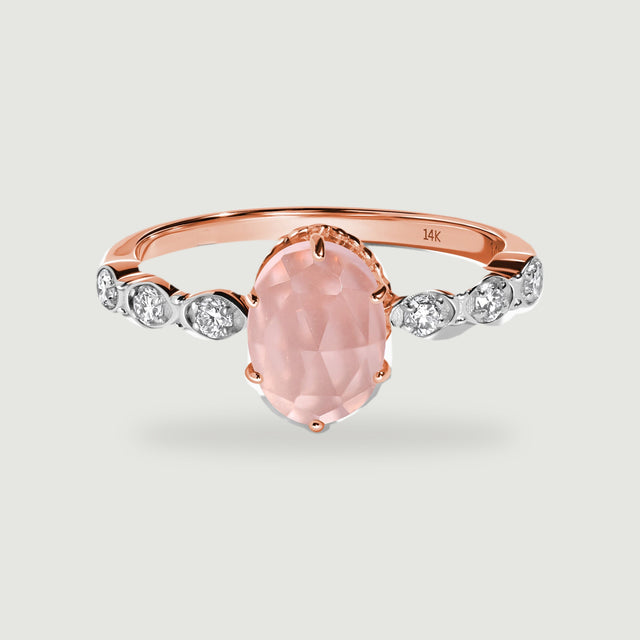 A rose gold ring with a faceted oval pink center stone and six diamond accents is centered above a soft contact shadow.