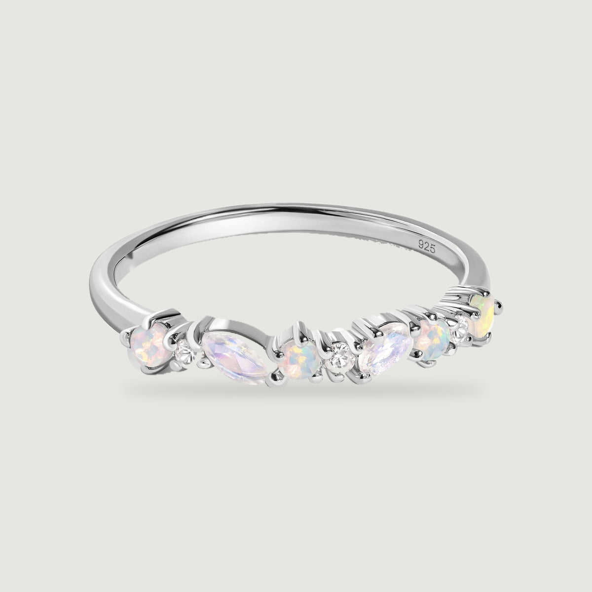 A polished silver ring displays pastel opals and elongated pale stones above a softly shadowed grey surface.