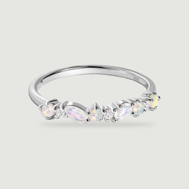A polished silver ring displays pastel opals and elongated pale stones above a softly shadowed grey surface.