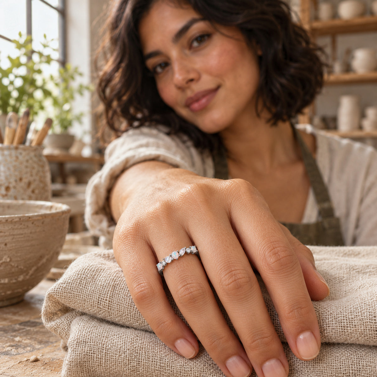 A silver gemstone ring is shown on a hand resting on folded linen in a pottery workshop.