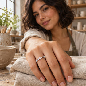 A silver gemstone ring is shown on a hand resting on folded linen in a pottery workshop.