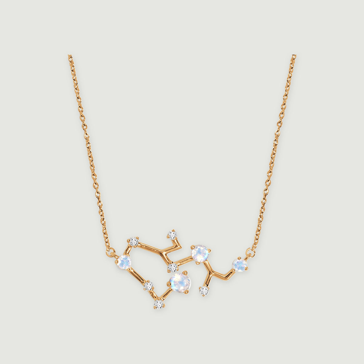 A yellow gold necklace has four iridescent round stones and small clear stones along an angular pendant on a light gray background.