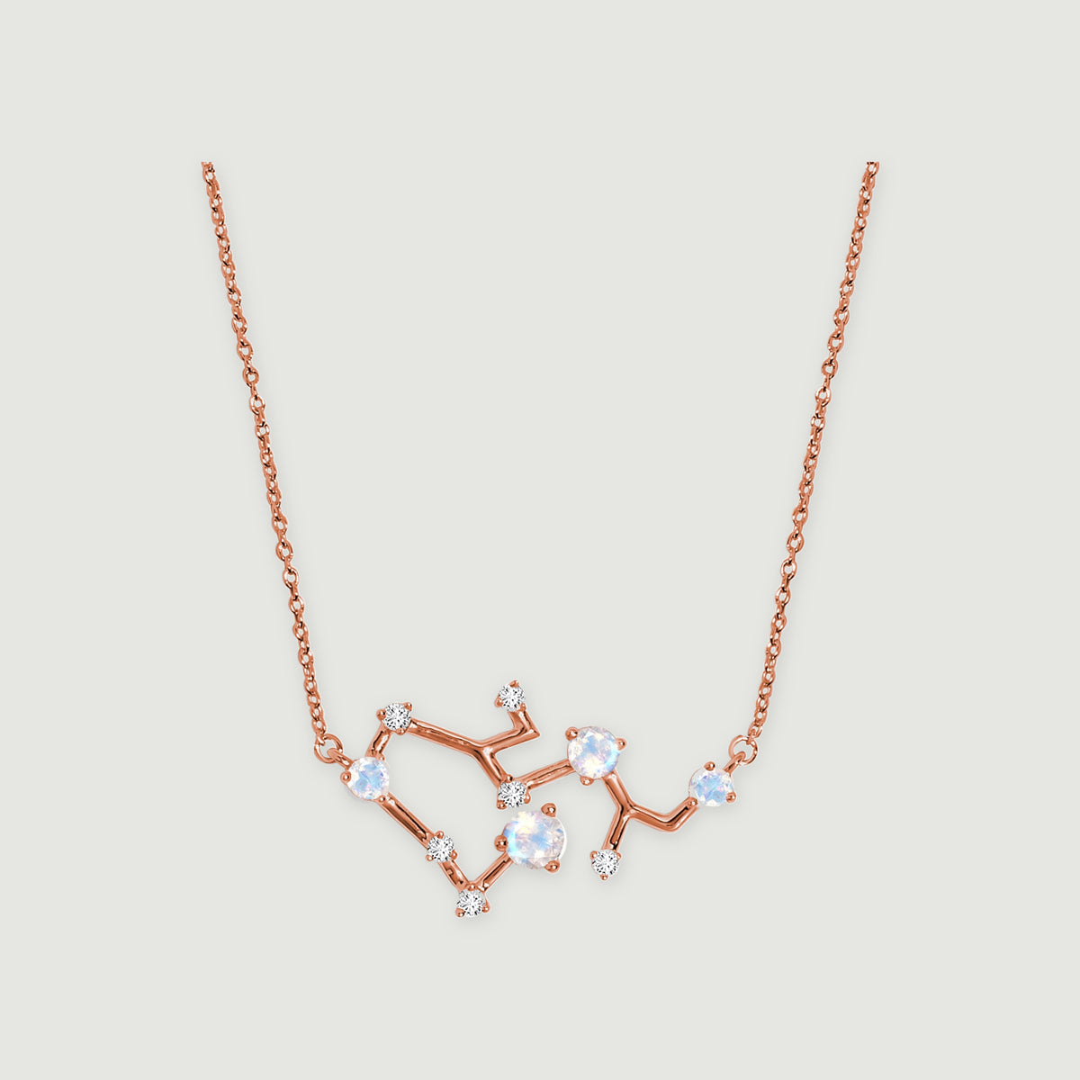 A rose gold necklace has four iridescent round stones and small clear stones along an angular pendant on a light gray background.