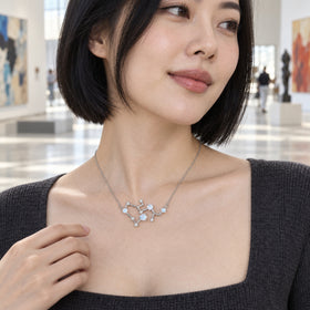 A woman with a black bob wears a silver necklace with an angular blue-white stone pendant above a charcoal neckline in an art gallery.