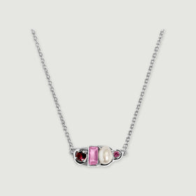 A sterling silver chain curves toward an asymmetric pendant with burgundy and pink stones beside a white pearl.