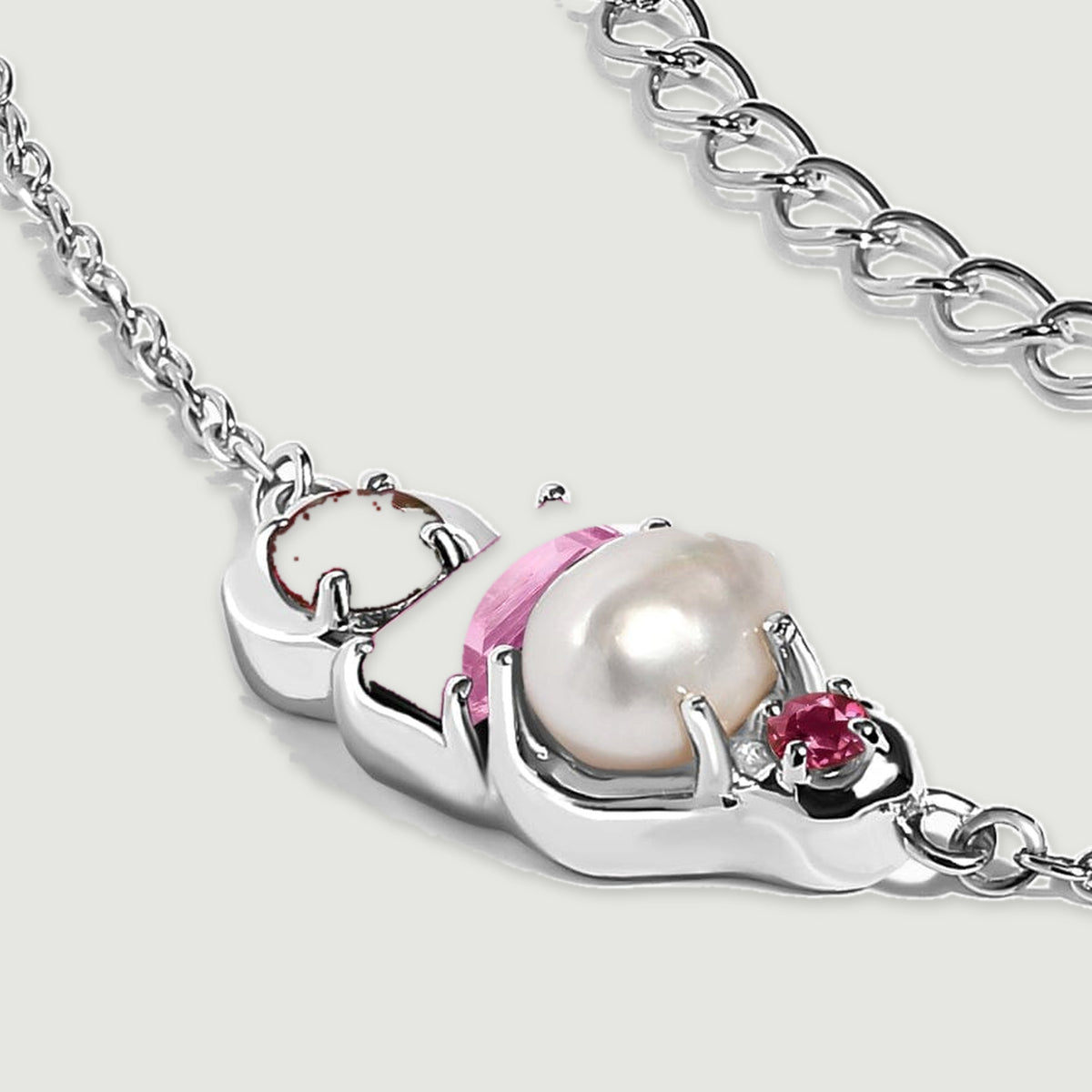 A silver pendant rests at an angle with its pearl held above a polished setting and a fine chain curving alongside it.