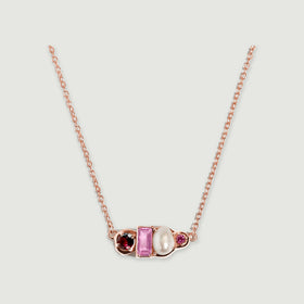 A rose gold vermeil necklace rests against a pale gray surface with its four differently shaped pendant elements facing forward.