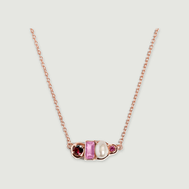 A rose gold vermeil necklace rests against a pale gray surface with its four differently shaped pendant elements facing forward.