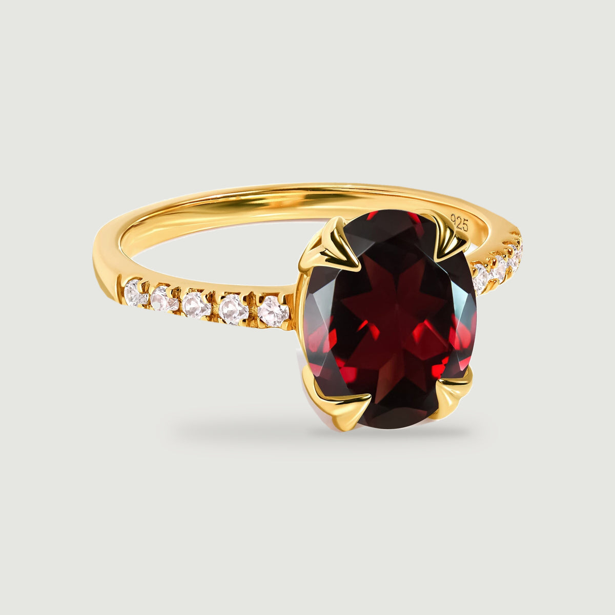 An oval deep red garnet sits in yellow gold prongs above a band lined with small clear stones.