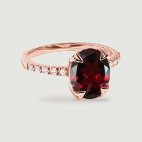Rose gold prongs hold a dark red oval gemstone on a slender stone-set band.