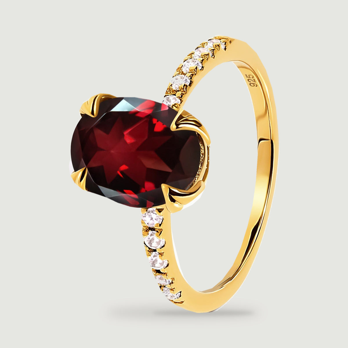 An angled yellow gold ring shows the garnet facets and clear stones along the raised shoulder.