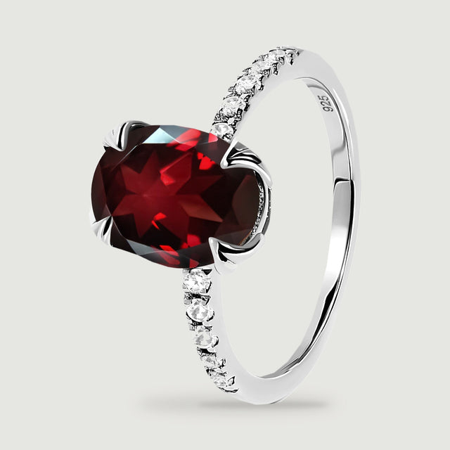 The silver ring stands at an angle with its red center stone and curved polished band visible.