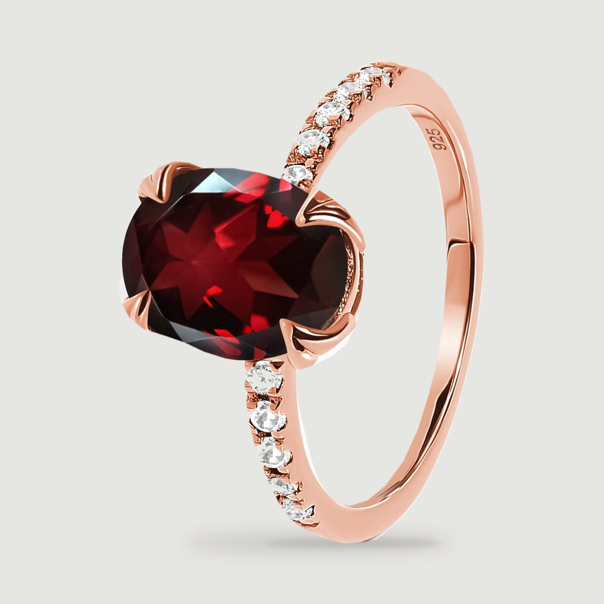 A tilted rose gold ring reveals four curved prongs around the garnet and clear accents down the band.