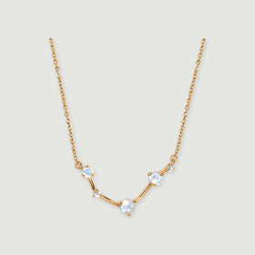A yellow gold necklace with three round iridescent stones and two small clear stones rests on a light grey surface.