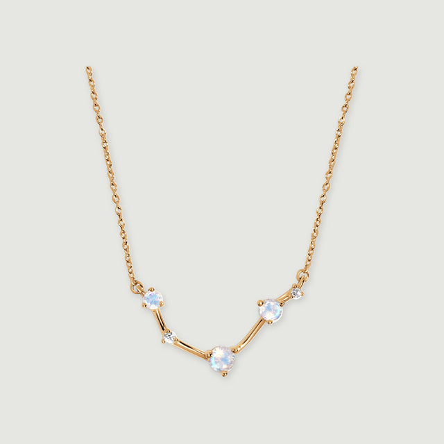 A yellow gold necklace with three round iridescent stones and two small clear stones rests on a light grey surface.