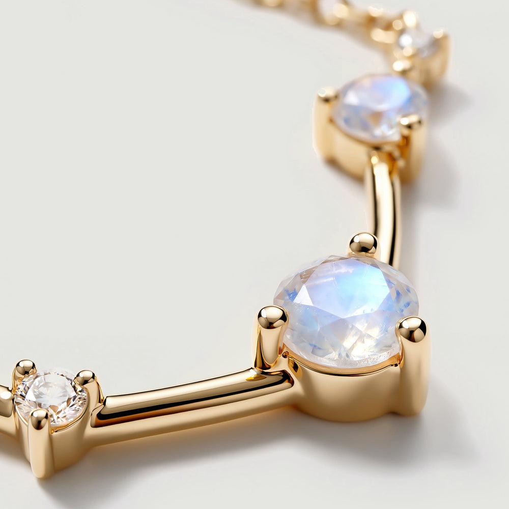 A close view shows a round iridescent stone held by gold prongs beside a small clear stone and polished connecting bars.