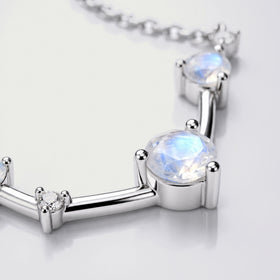 A blue-flashing round stone and a small clear stone sit in silver settings joined by polished bars.