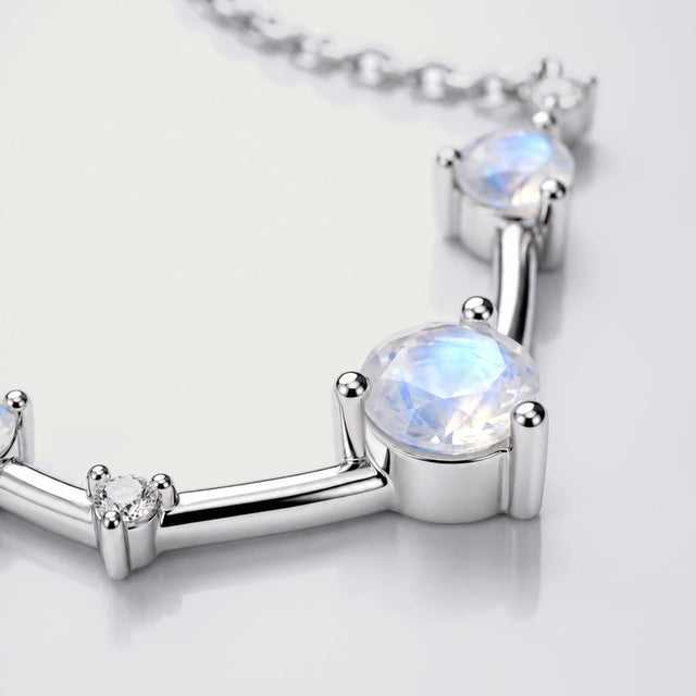 A blue-flashing round stone and a small clear stone sit in silver settings joined by polished bars.