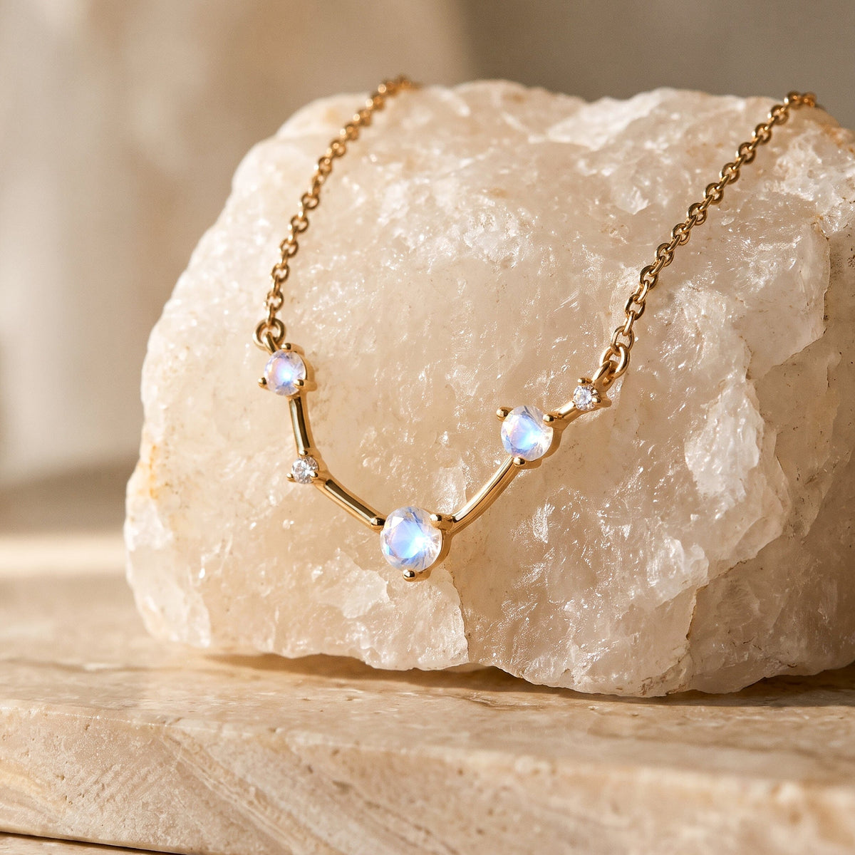 The gold necklace is draped across a pale textured stone on a clean beige tabletop.