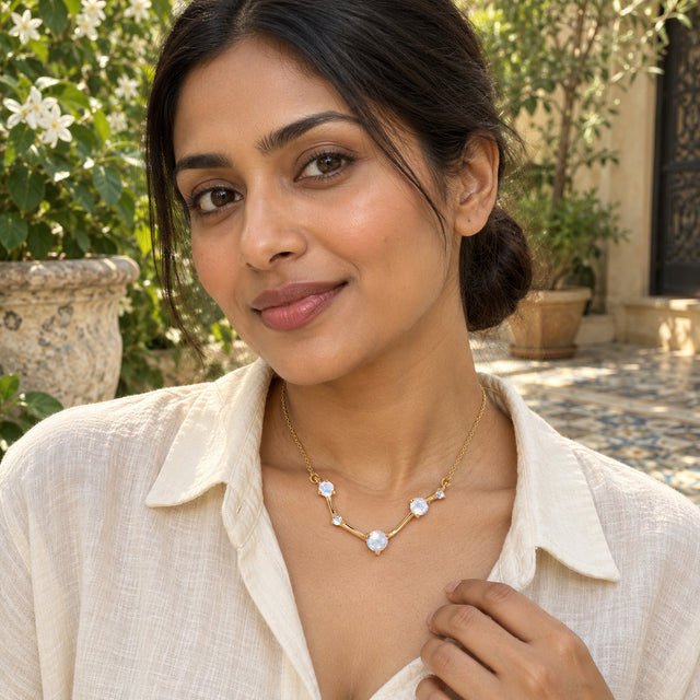 A woman in a cream linen shirt wears the yellow gold necklace in a leafy tiled courtyard.