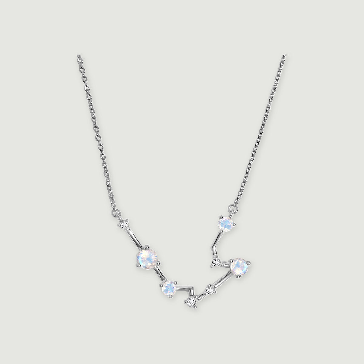 A silver chain frames a curved constellation of pale round moonstones and small clear stones on a light gray surface.