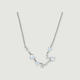 A silver chain frames a curved constellation of pale round moonstones and small clear stones on a light gray surface.