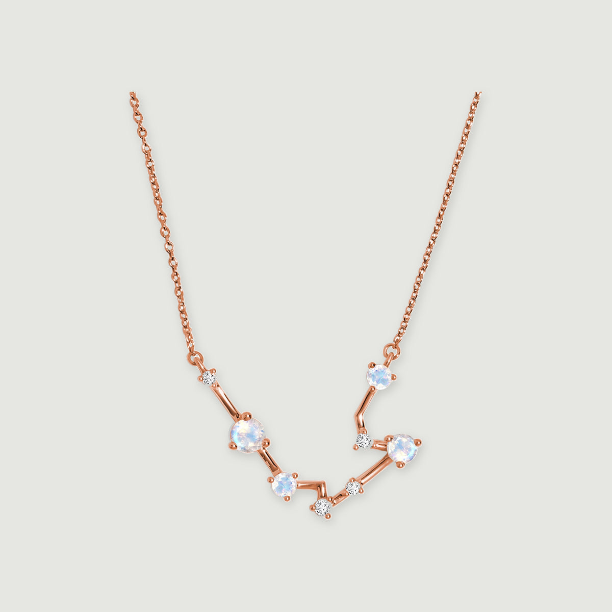 A rose gold chain joins a shallow arc of blue white moonstones and tiny clear accents on light gray.