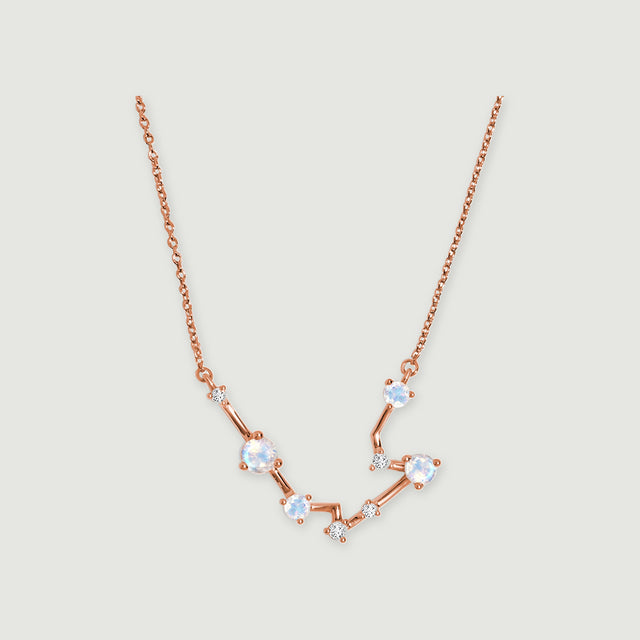 A rose gold chain joins a shallow arc of blue white moonstones and tiny clear accents on light gray.