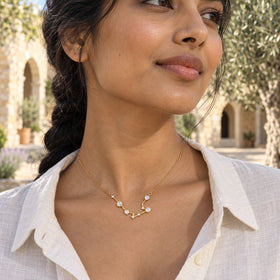 A delicate yellow gold moonstone necklace sits inside an ivory linen collar in a sunlit stone courtyard.