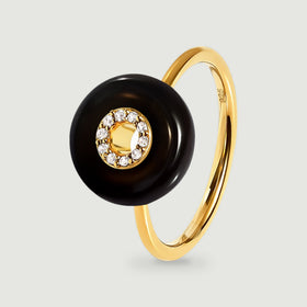 A yellow gold vermeil ring with a black circular stone and clear stones around the center stands on a light gray surface.