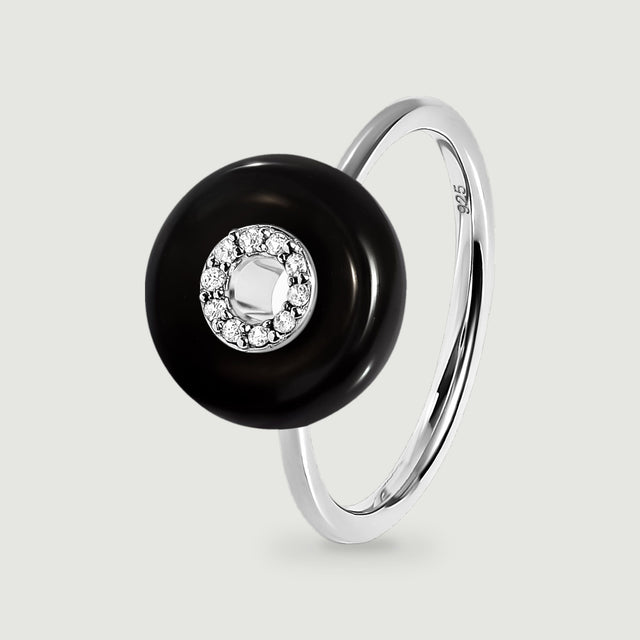 A sterling silver ring with a polished black disc and a circle of clear stones is shown upright against light gray.